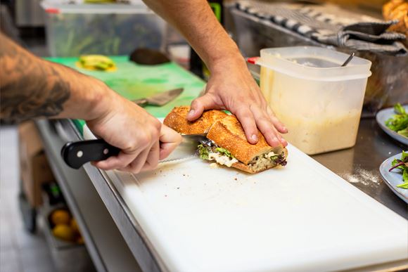 Ein Koch schneidet ein Baguette mit einem Messer in der Mitte durch.